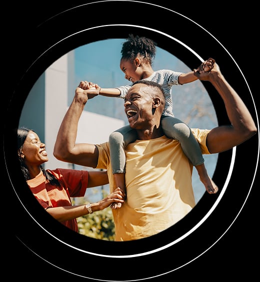 Joyful family moment: a child rides on a man's shoulders while holding hands with a smiling woman outdoors.