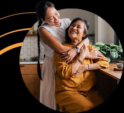 A young woman hugging an elderly woman in a kitchen setting, both smiling warmly